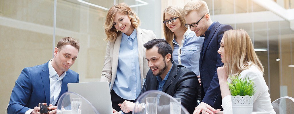 Ein Team von Frauen und Männern schaut sich einen Bericht auf einem Laptop an